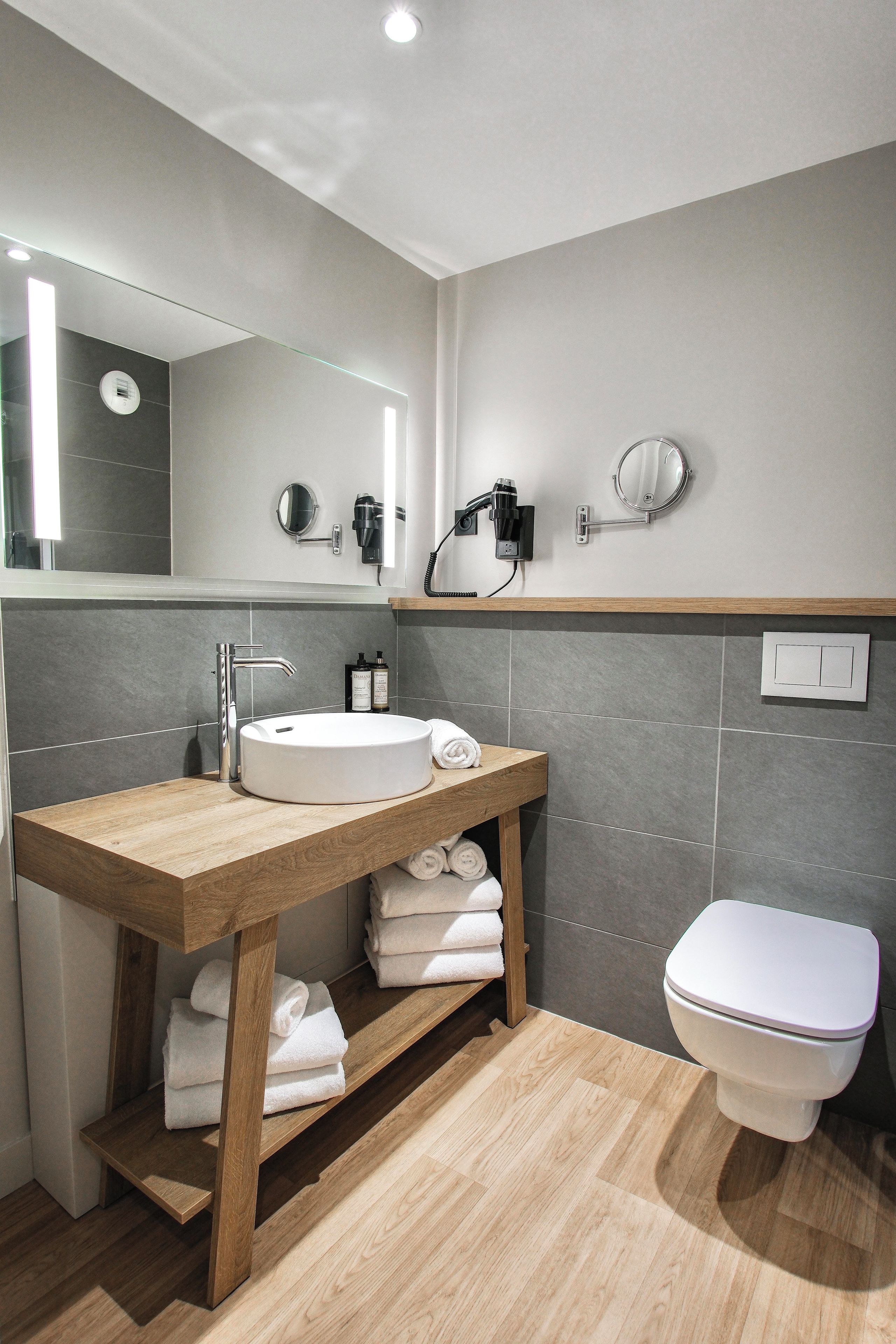 Un baño moderno con tocador de madera, espejo redondo, inodoro y barra para toallas.
