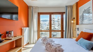 Une chambre d’hôtel avec un grand lit, un bureau équipé d’un ordinateur et une vue sur des arbres couverts de neige.
