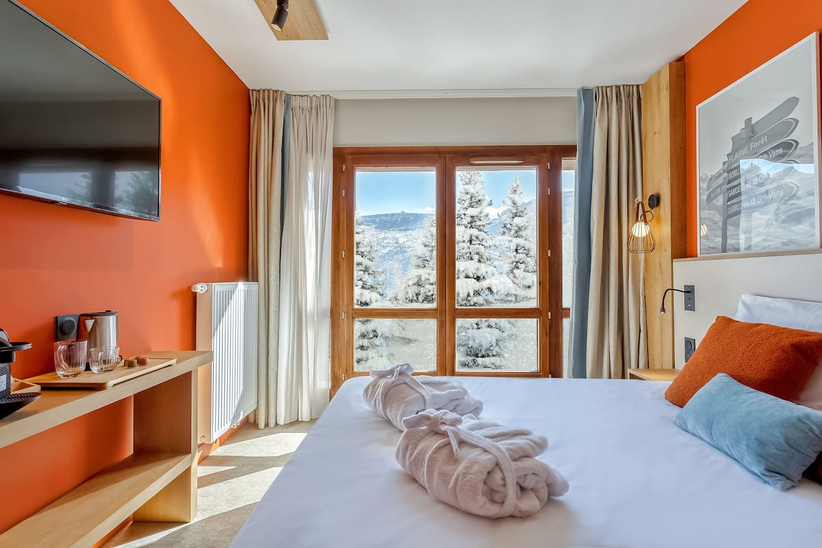 Habitación de hotel con una cama grande, un escritorio con ordenador y vistas a árboles cubiertos de nieve.