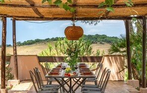 An outdoor dining area with a table set for six, surrounded by chairs, under a wooden pergola with a hanging light fixture. - 6 bedroom nice home in Grosseto (Grosseto)