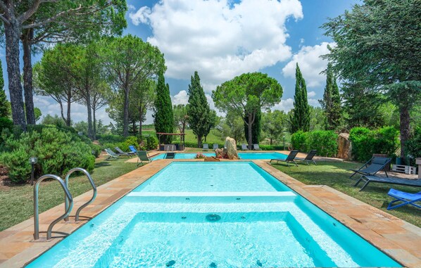 A rectangular swimming pool with a stone border, surrounded by lounge chairs and trees. - 6 bedroom nice home in Grosseto (Grosseto)