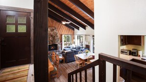 Ein gemütliches Wohnzimmer mit Kamin aus Stein, Holzbalkendecke und einem Essbereich mit Tisch und Stühlen.