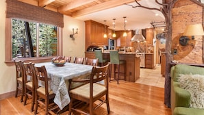 Une cuisine chaleureuse avec des meubles en bois, un coin repas comprenant une table et des chaises, et une vue sur l’extérieur grâce à de grandes fenêtres.