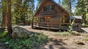 Une cabane en bois dotée d’un balcon, entourée d’arbres et de rochers.