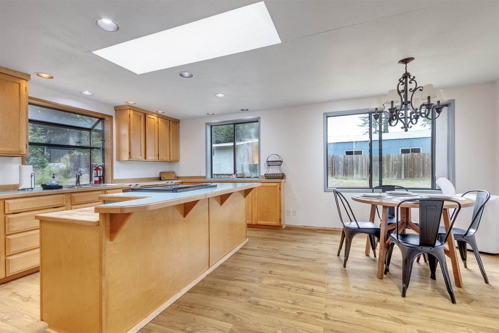 A modern kitchen with wooden cabinets, a central island, and a dining area with chairs and a table.