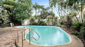 Una piscina rectangular con una escalera metálica, rodeada de diversas plantas y árboles tropicales.