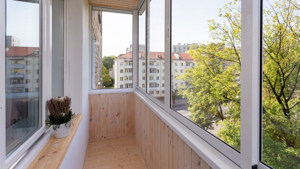 A balcony with large windows, wooden floor, and a potted plant. - Apartment in the heart of Minsk (Minsk)