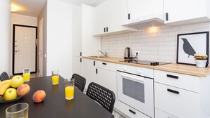 A modern kitchen with white cabinets, a wooden countertop, and a black chair. There is a fruit bowl with apples and peaches, and a glass of orange juice on the table. - Apartment in the heart of Minsk (Minsk)
