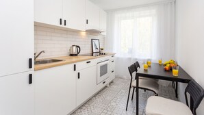 A modern kitchen with white cabinets, a wooden countertop, a stainless steel sink, and a small oven. There is a dining table with chairs and a fruit bowl with oranges and bananas. - Apartment in the heart of Minsk (Minsk)