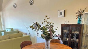 Un comedor con una mesa redonda de madera, cuatro sillas, un florero con flores, un aparador con puertas de vidrio y una alfombra colorida.