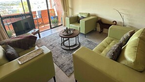 Una sala de estar con sofá, sillones, una mesa de centro y vistas amplias a través de ventanas grandes.