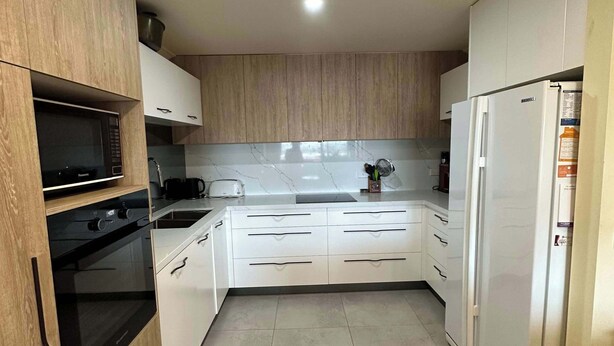 Una cocina moderna con armarios de madera, horno empotrado, microondas y refrigerador.