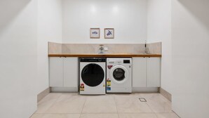 Una sala de bugaderia amb dues rentadores, un taulell de fusta i dos quadres penjats a la paret.