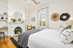 A bedroom with a fireplace, a bed with pillows, a chair, and a mirror.
