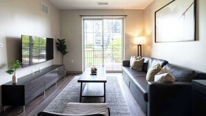 A modern living room with a sofa, a coffee table, a TV, and a large window with a view of buildings.