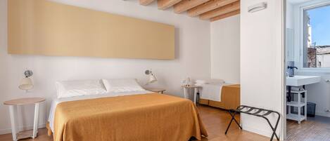 A bedroom with a large bed, a bedside table, a nightstand, a hanging light, and a view of the city through a window.