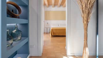 Un dormitorio moderno con suelo de madera, cama con colcha color beige y un ventanal grande.