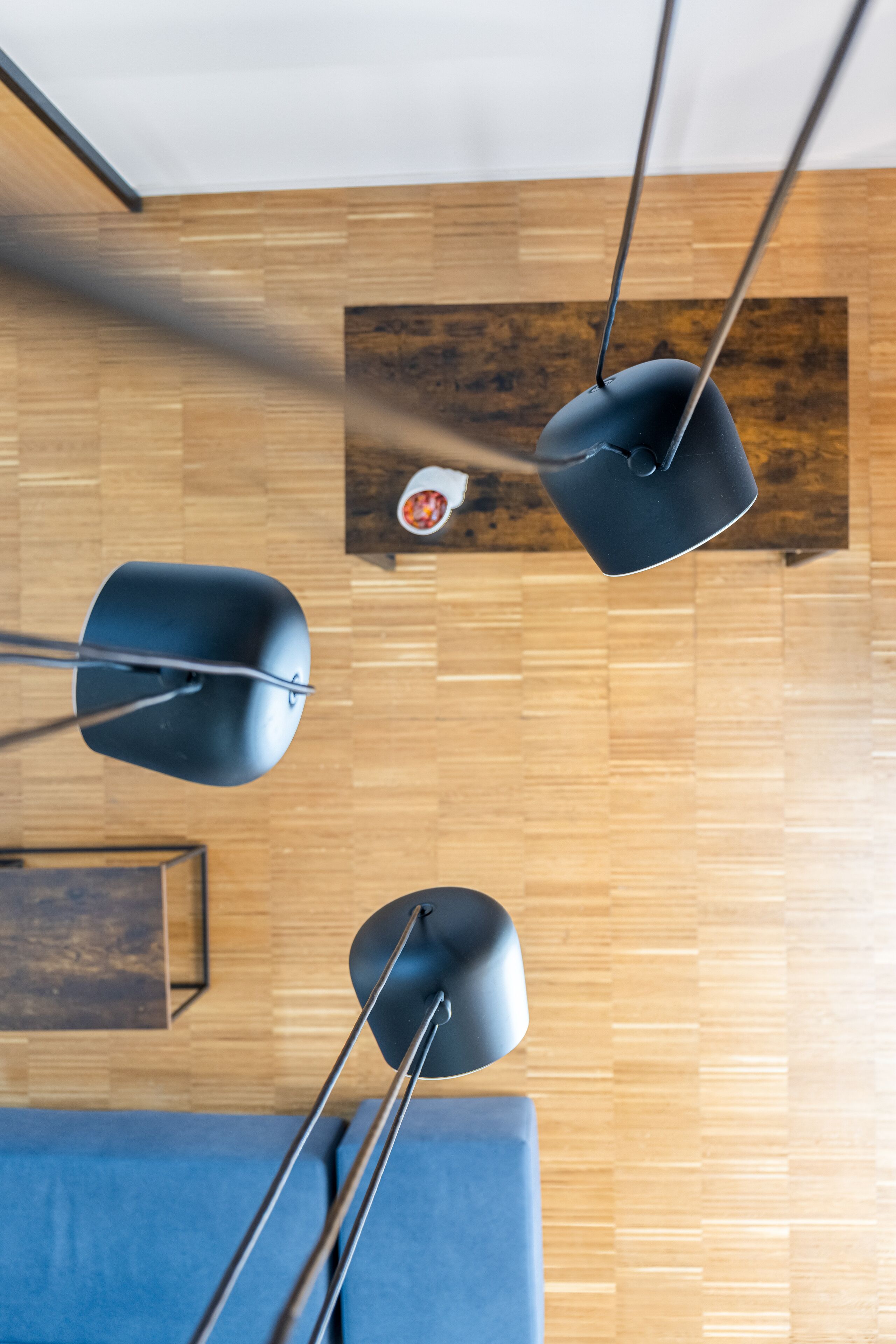 Un interno moderno con pavimento in legno, un divano blu e tre lampade a sospensione nere.