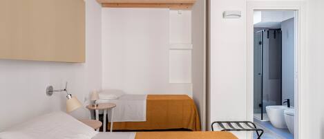 A hotel room with a bed, bedside table, lamp, and a view of the bathroom.