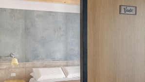 A bedroom with a bed, a round wooden table, a wall-mounted light, and a door with a sign reading "Vento". - Le Stanze di Triyah (Palermo)