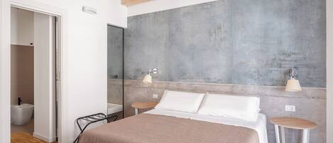 Een moderne slaapkamer met een groot bed, nachtkastjes, een spiegel en een betonnen accentmuur.