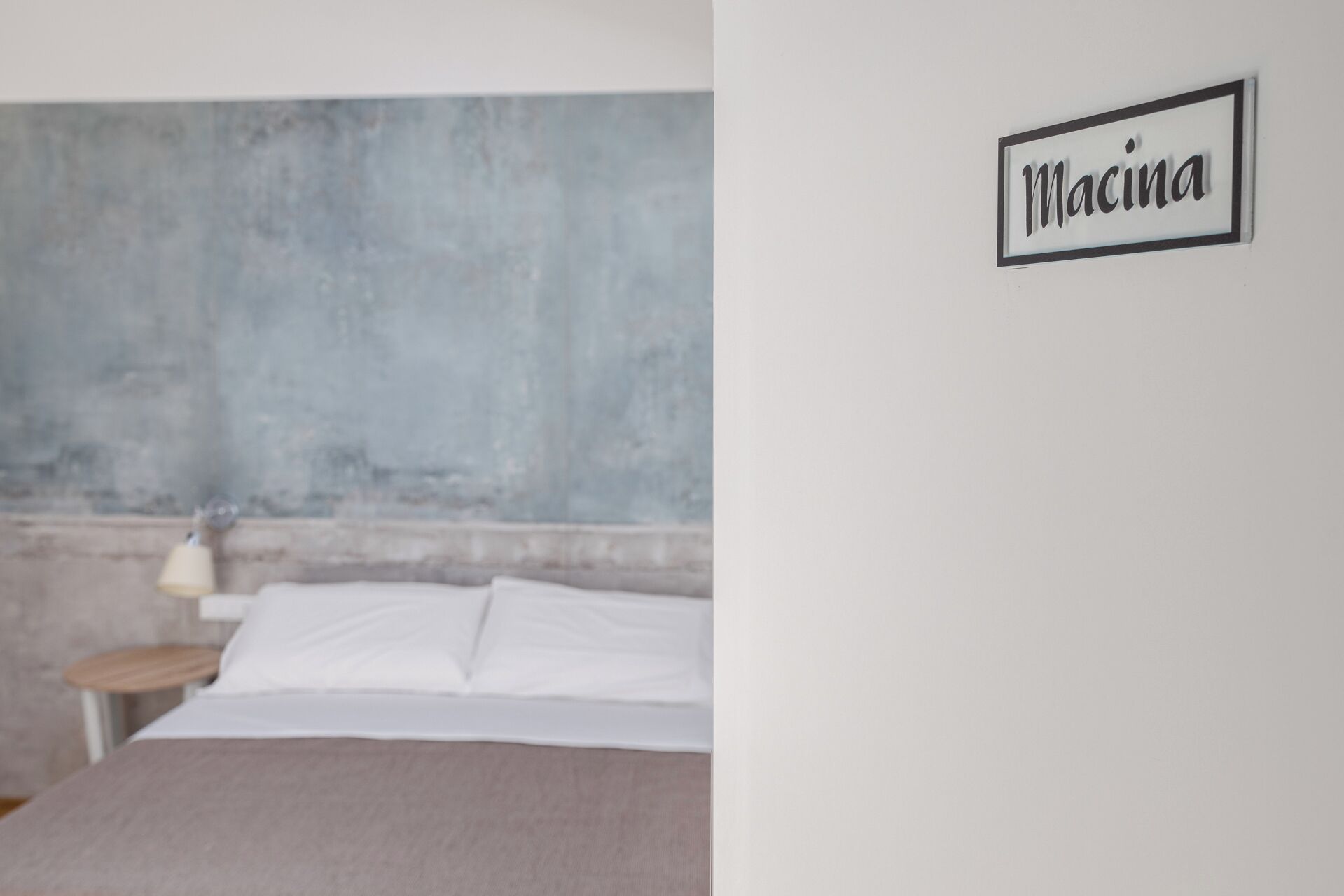 Une chambre à coucher avec un lit, une table de chevet et un panneau fixé au mur sur lequel on peut lire « Macinia ».