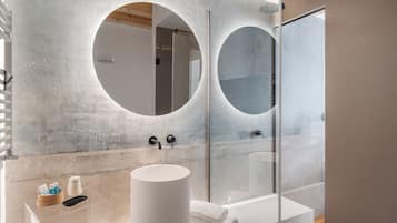 A modern bathroom with a large round mirror, a bathtub, and a glass-enclosed shower.