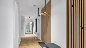 A modern hallway with wooden flooring, a grey bench, a wall-mounted wooden slat panel, and a hanging wooden rack. - GebirgsResort Winterberg (Winterberg)