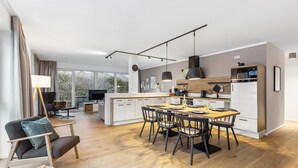 A modern kitchen with a central island, dining area with chairs, and a TV in the living room. - GebirgsResort Winterberg (Winterberg)