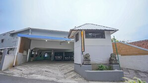 A building with a garage entrance, a blue awning, and a small structure with a tiled facade. - Hotel O Lie Mas Hotel (Prigen)