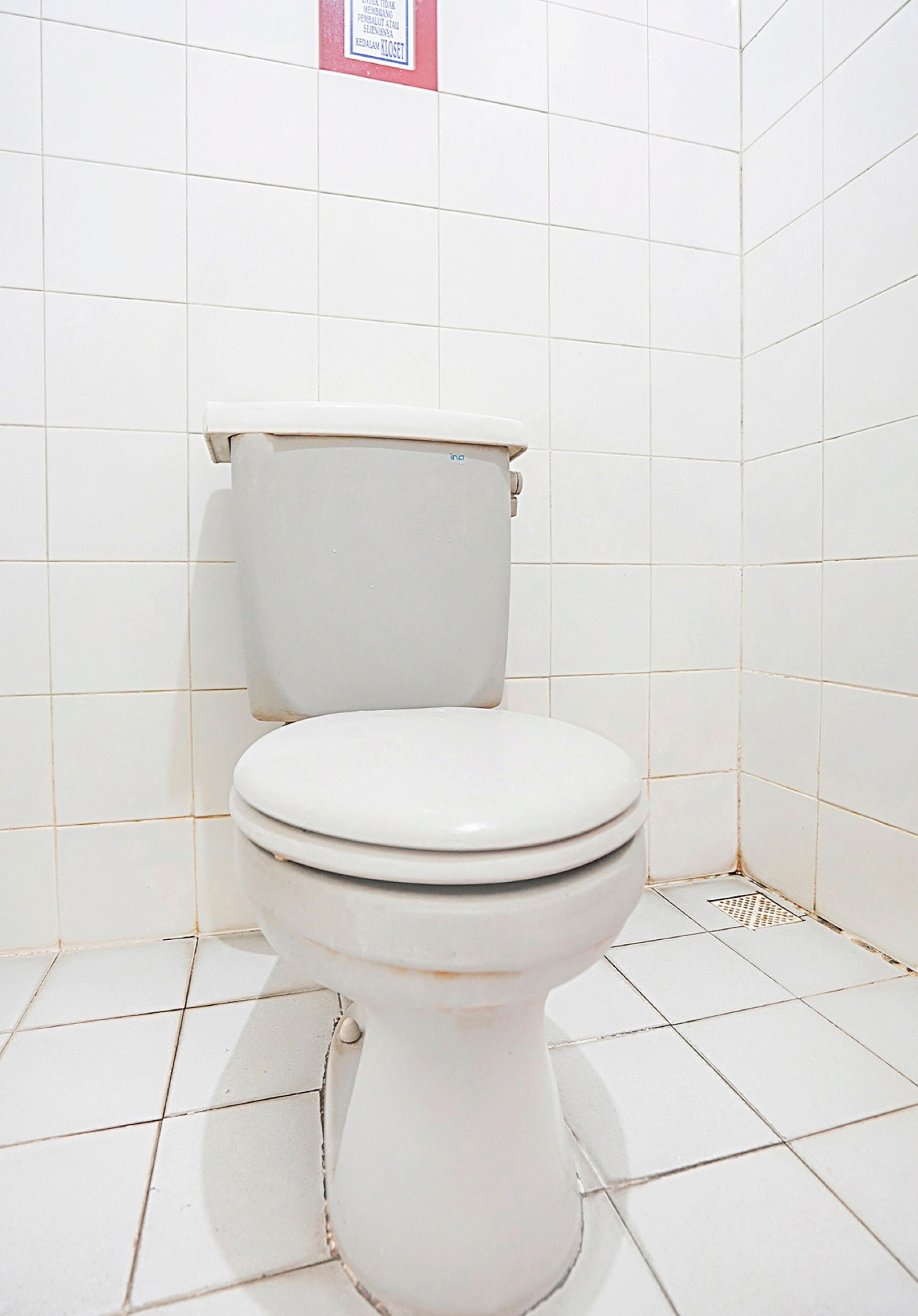 A white toilet in a bathroom with white tiled walls and floor.