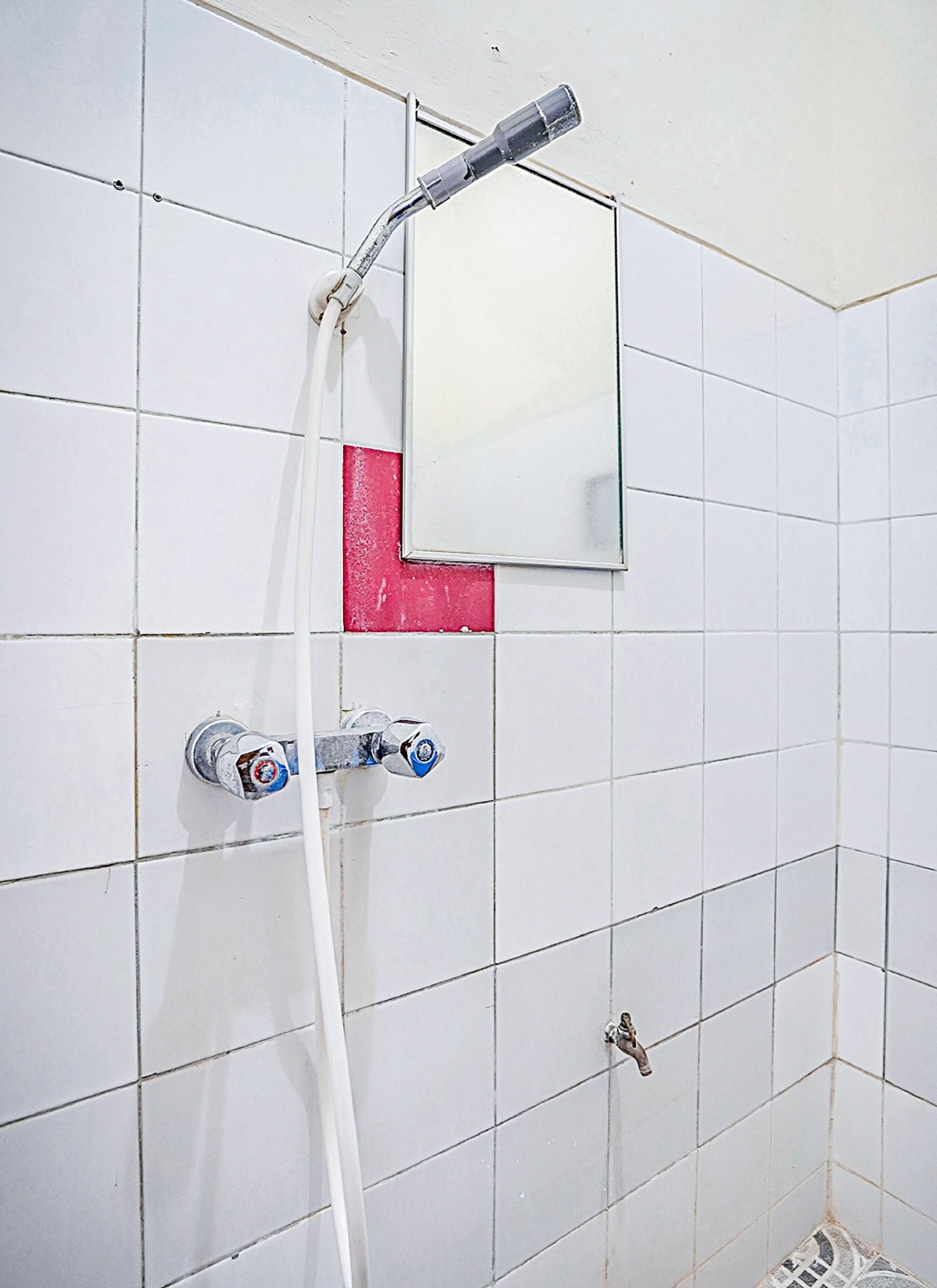 Un baño con paredes de azulejos blancos, un cabezal de ducha y dos llaves.
