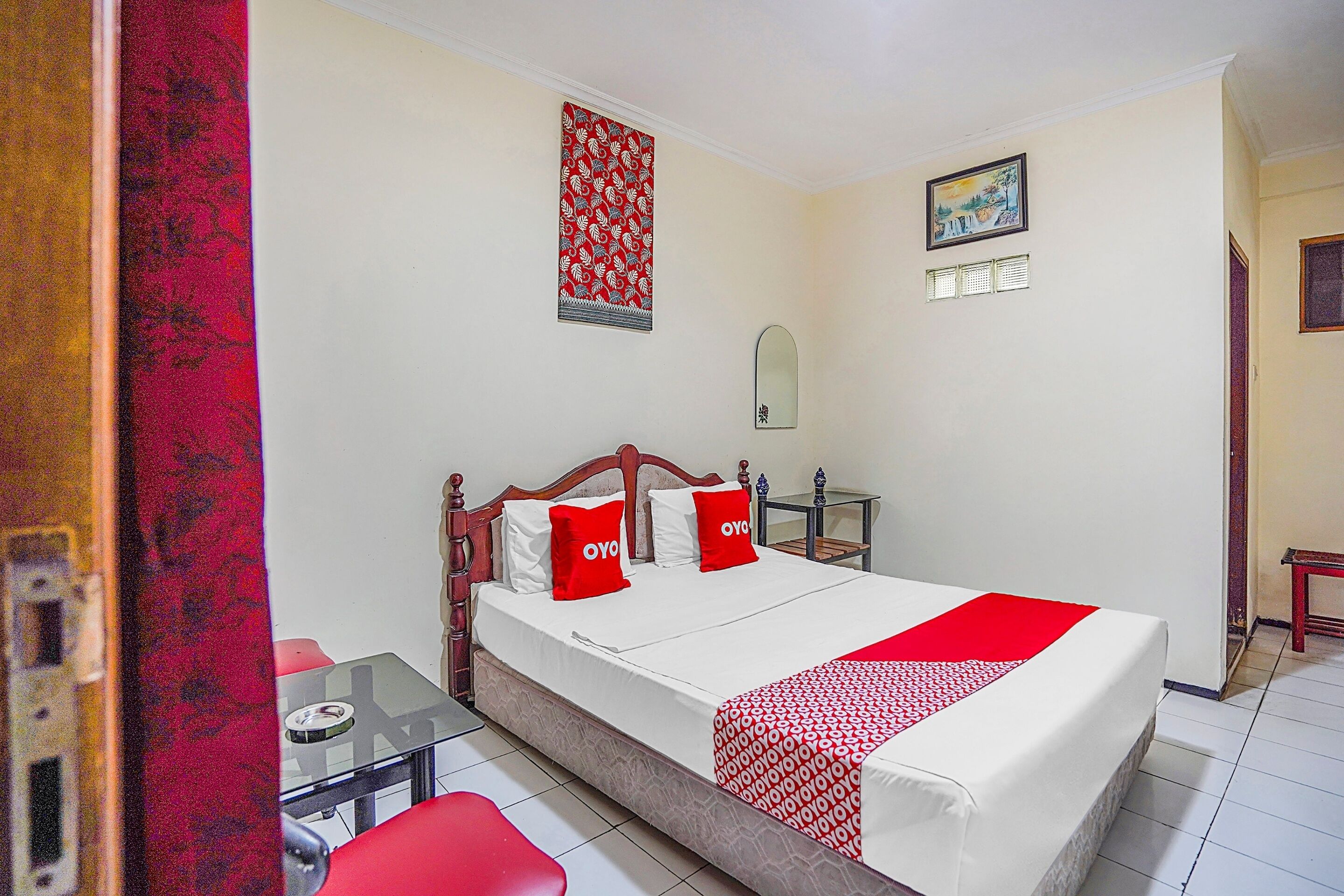 Habitación de hotel con cama, una mesita, una silla, un espejo y un cuadro en la pared.