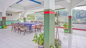 A spacious indoor area with a long table and chairs, surrounded by potted plants and a balcony with a scenic view. - Hotel O Lie Mas Hotel (Prigen)