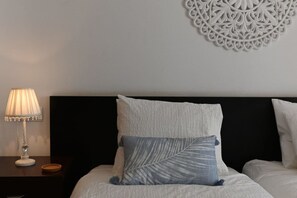 A neatly made bed with a white headboard and two pillows, one with a leaf pattern.