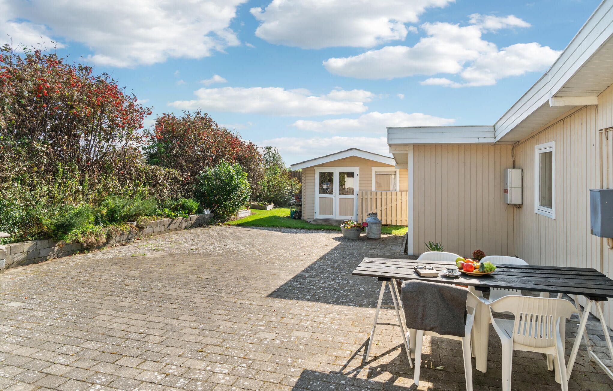 En terrasse med et bord og stole, en lille have og en bygning med dør og vinduer.