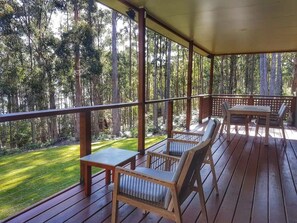A covered outdoor area with wooden furniture and a view of a forest.