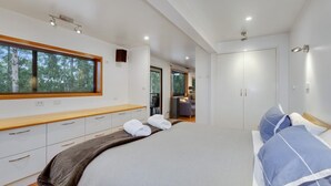 Ein modernes Schlafzimmer mit einem großen Bett, einer Holzbank, einem Kleiderschrank und einem Fenster mit Blick auf Bäume.