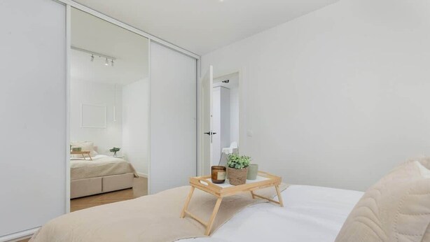 Un dormitorio con una cama, una mesita de noche con una bandeja, un espejo y una puerta corredera que da a otra habitación.