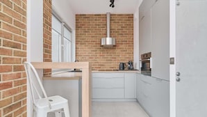 A compact kitchen with a brick wall, a stainless steel range hood, a coffee maker, and a white chair. - Sunny Apartment | Balcony | Parking | Workspace. (Wrocław)