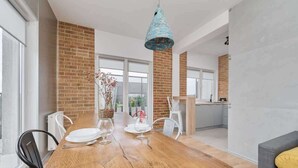 A dining area with a wooden table, white chairs, a hanging light fixture, and a brick wall. - Sunny Apartment | Balcony | Parking | Workspace. (Wrocław)