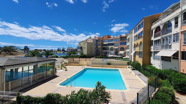 Une piscine entourée d’immeubles à plusieurs étages dotés de balcons, un ciel bleu dégagé et quelques espaces verts.