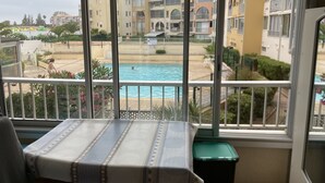 Un balcon donnant sur une piscine, une table recouverte d’une nappe et une poubelle.