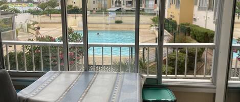 A balcony with a view of a swimming pool, a table with a tablecloth, and a trash bin.