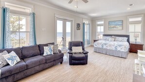 A spacious bedroom with a large bed, a sitting area with a sofa and armchair, and a balcony with curtains. - Gulfport's Premier Beachfront Getaway, Ocean View Beach House! Sleeps 10 (Gulfport)
