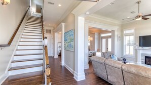 A spacious living area with a wooden staircase, a beige sofa, and a fireplace. - Gulfport's Premier Beachfront Getaway, Ocean View Beach House! Sleeps 10 (Gulfport)