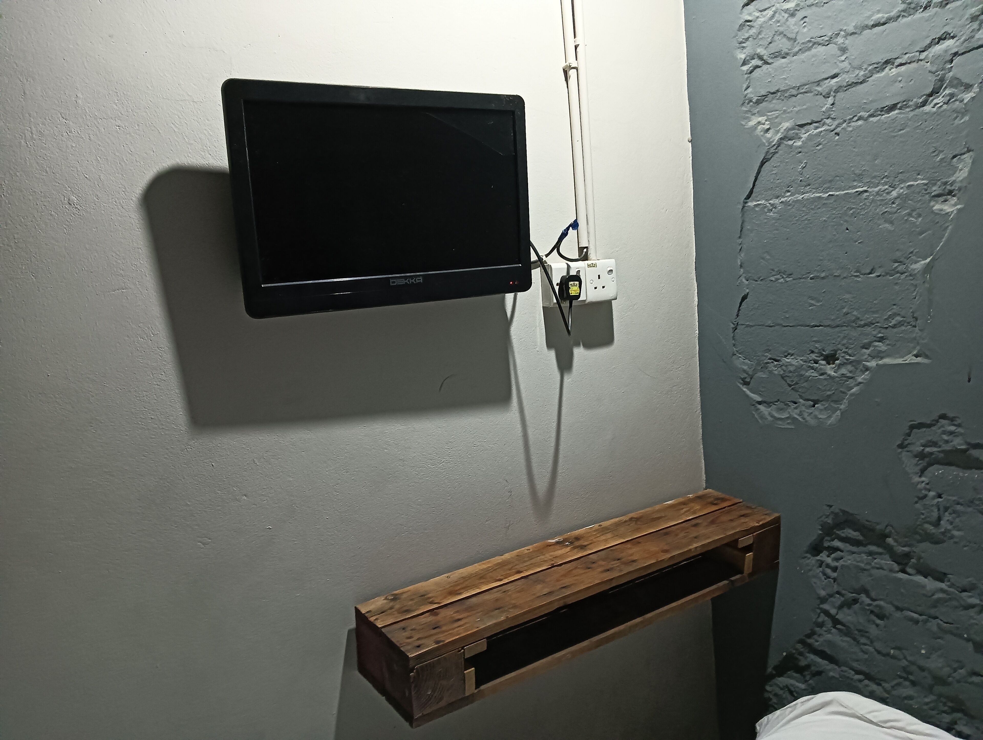 A television mounted on a wall with a wooden shelf below it.