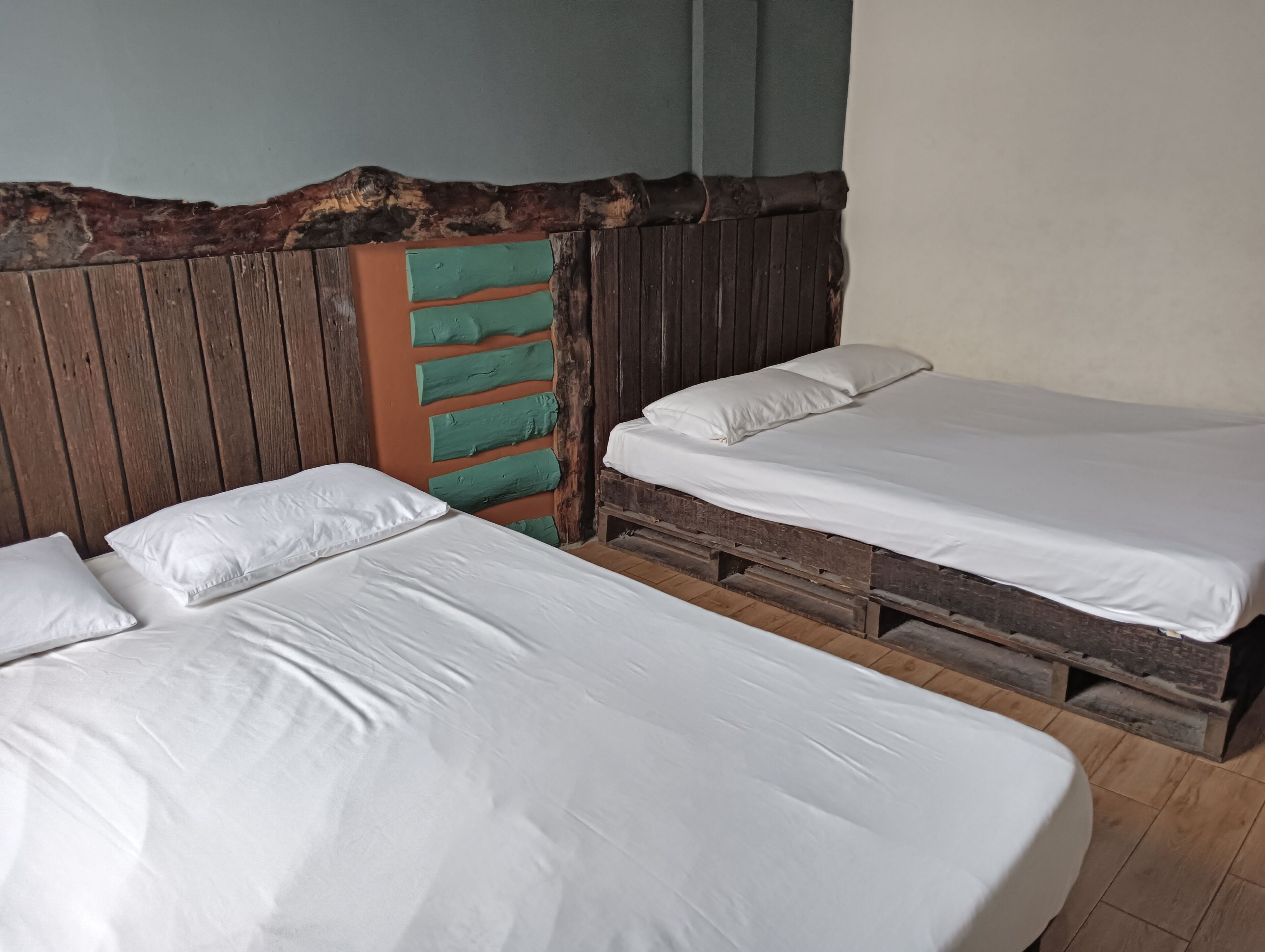 Une chambre avec deux lits, une tête de lit en bois et un mur d’accent vert.