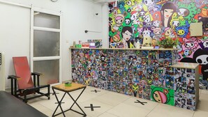 A room with a colorful wall covered in cartoon characters, a red chair, a small wooden table, and a black couch.
