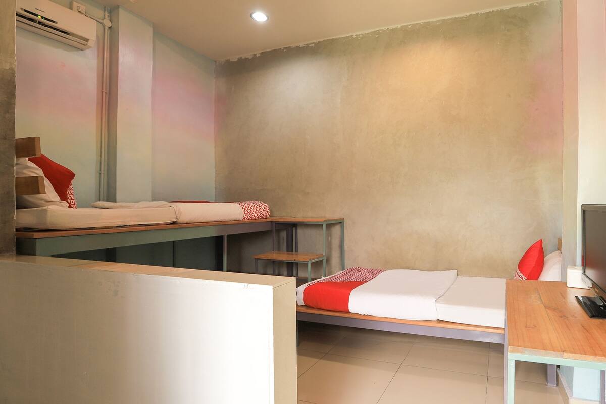 A room with bunk beds, a desk, a chair, a TV, and an air conditioning unit.